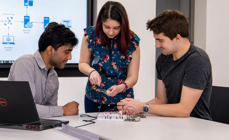 Three computer science students working with a motherboard of a computer