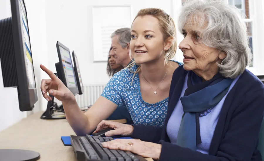 Several students sitting in pairs with elderly people, working together at computers.