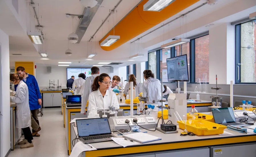 Group of students working in a bright, modern, vibrant chemistry laboratory. Students tend to a variety of equipment and glassware on the benches.