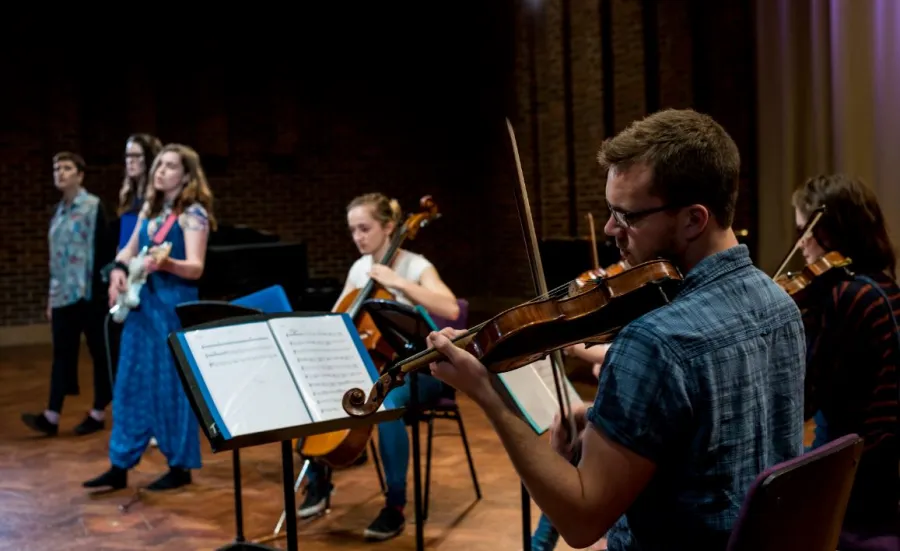 A violinist in foreground with musicians behind performing in Turner Sims