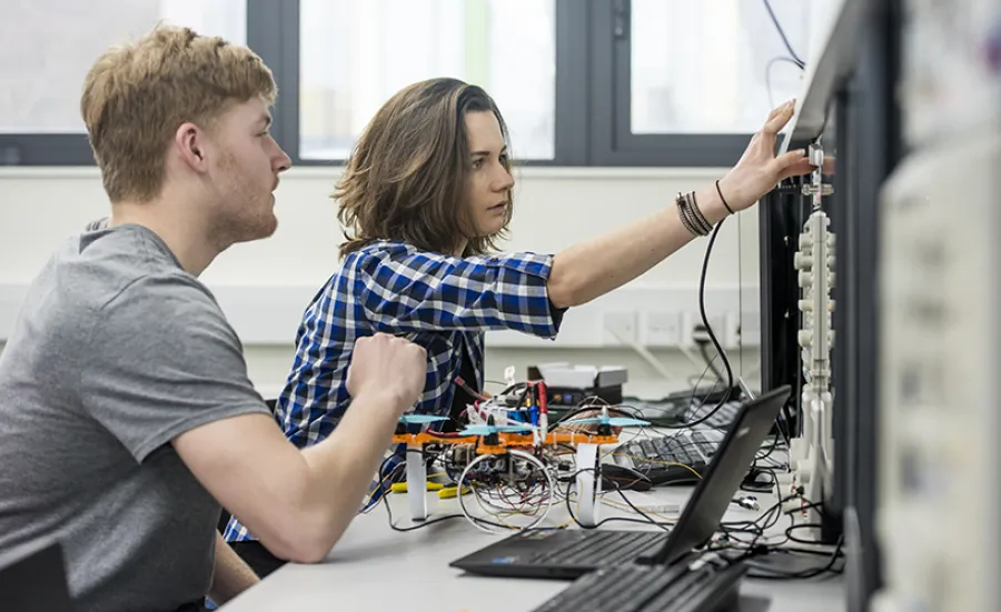 Two students working on the electronics of a small drone, at a workbench in the teaching lab.