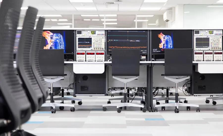 A wide shot of various work benches in the laboratory, featuring high-definition monitors and specialised testing equipment.