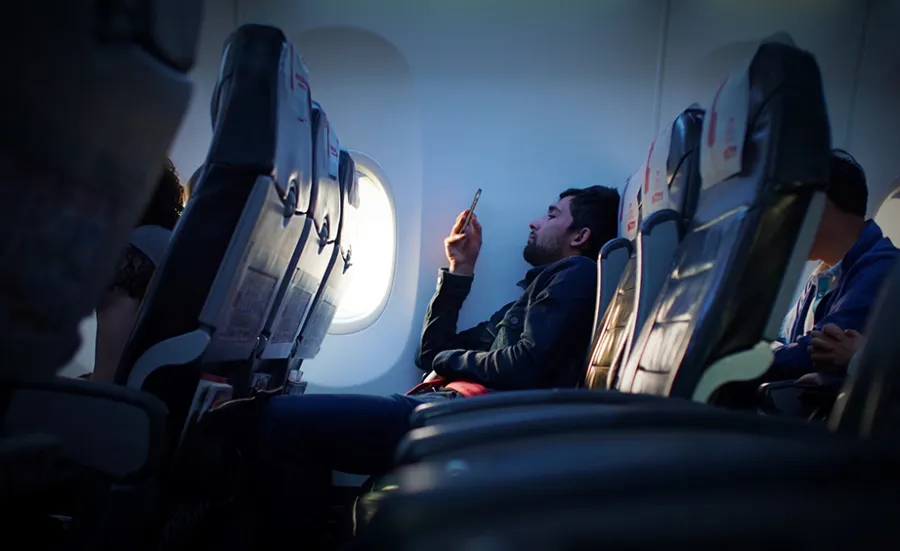 A man looks at his mobile phone while seated on a plane flight