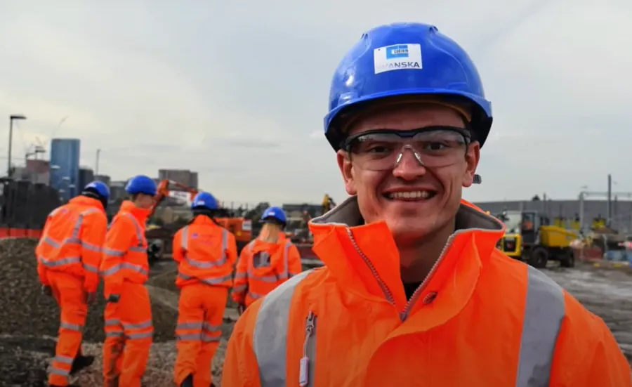 A group of engineering students in overalls and hard hats in an industrial setting