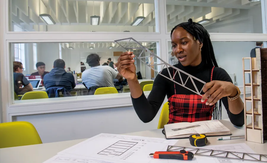 Civil engineering student Virtue, a young Black woman, works on a design at a desk in our campus building, immersed in her work