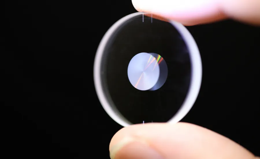 A small optical lens held between a finger and thumb