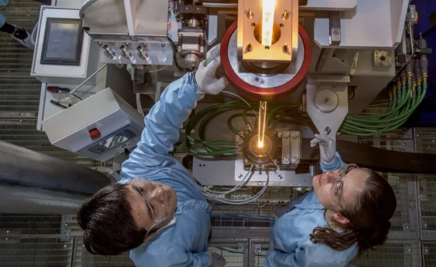 View from above of two researchers feeding glass into a fibre drawing furnace.