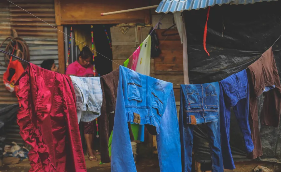 Woman walking past numerous people sitting along a fence covered in laundry