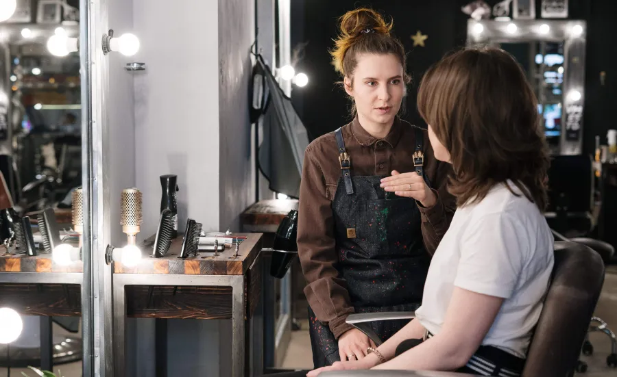 A hair stylist talking with a client in a salon