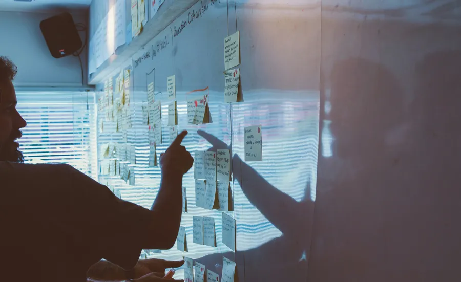 Unsplash image of post-its on a white board, a meeting participant points to a note