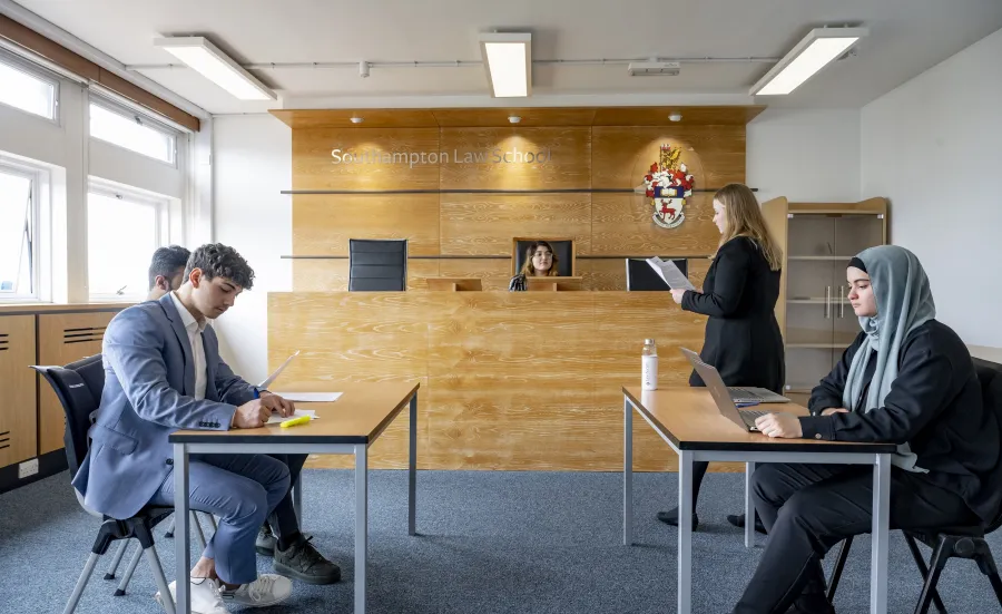 A group of 5 smartly dressed law students practise a court case in a mock courtroom.