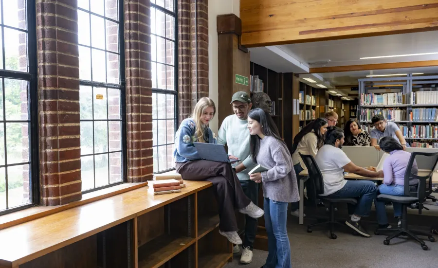 Two groups of students in the Hartley library. I group looking at a laptop and the other talking around a table.