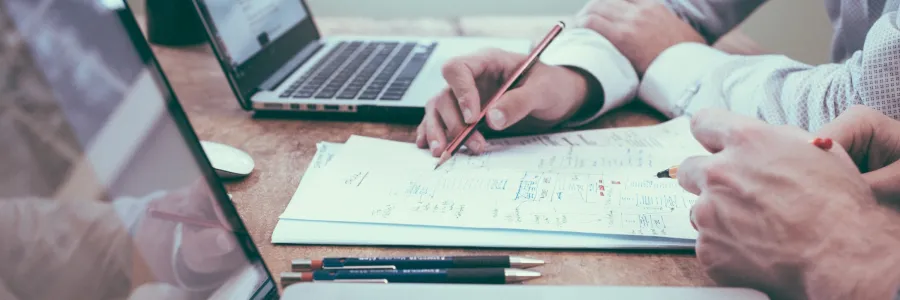 Close up view of two people working at a desk with laptops, paper and pens