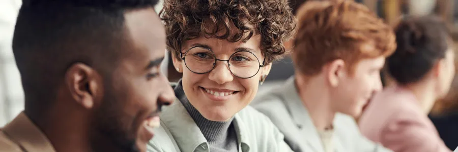 Two individuals smiling and reviewing a document together, with others in soft focus in the background, suggesting a collaborative work environment.