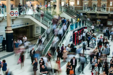 Many people in train station with stairs.