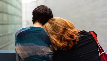 Two people sitting down, facing away from us. One is leaning into the other.