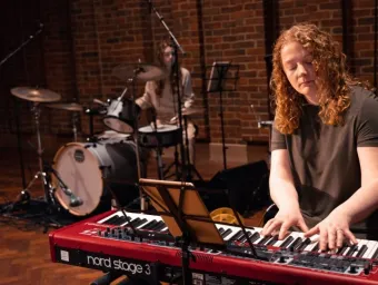 Two young musicians perform at the Turner Sims concert hall. The person in the foreground plays the keyboards, the person behind plays the drums.