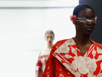 A catwalk model sports a dramatic red and white creation featuring a floral motif and outsized lapels