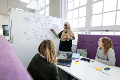 3 students in a common learning space, gathered around a whiteboard showing a mind map they are using to capture and organise their thoughts.