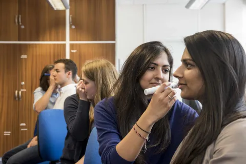 Several students in partner groups, inspecting each others' ears with an otoscope.