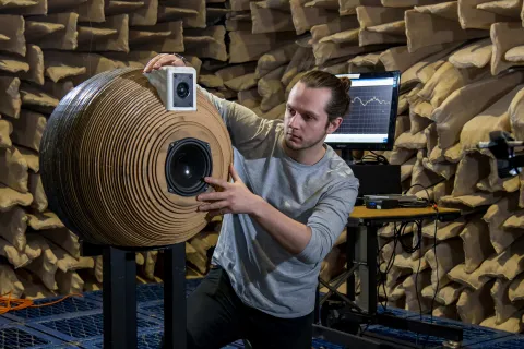 A student positioning a novel, spherically-designed speaker system inside the large anechoic chamber for testing.