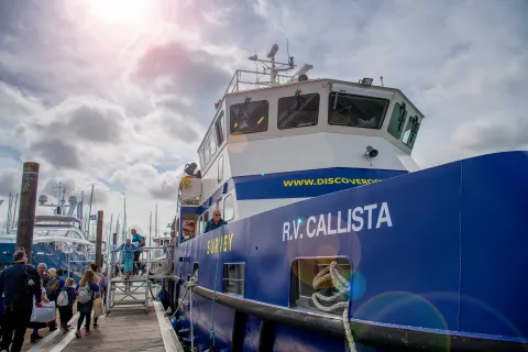 An industrial looking boat emblazoned with the name RV Callista, moored beside a wooden dock, beneath a sunny sky.