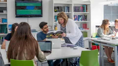 A lecturer teaching law students with laptops and text books in small groups