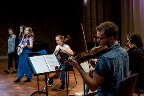 A violinist in foreground with musicians behind performing in Turner Sims