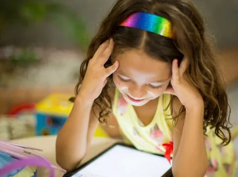 A young girl studies a tablet screen at a table