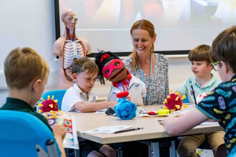 A group of primary school students doing educational activities around a table, with supervision from a member of staff.