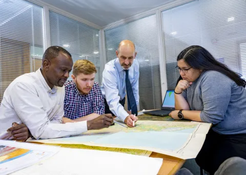 A ƱAPP_ĿͲƱ-ٷϷ, Geospatial researcher points to a map as he stands over colleagues from the team