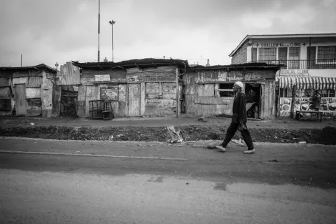 A black and white image of an elderly gentleman walking past a row of businesses in Nairobi, Kenya.