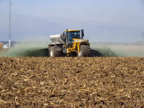 A tractor scattering crushed rock as it drives across a field.