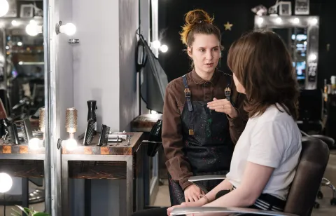 A hair stylist talking with a client in a salon