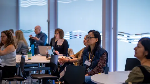 A group of people are sitting in a meeting room, looking at something that is out of frame to the left. 