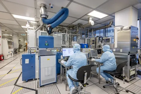 Two men in full cleanrooms uniforms are sitting at the desks working with equipment