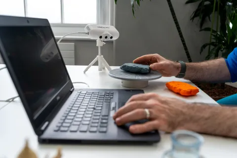 Open laptop on a desk with an unseen user, bar their wrists, operating the keyboard.