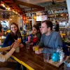 Group of students sat at table in a restaurant bar, talking and laughing over drinks.