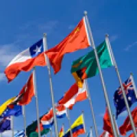 A collection of national flags flapping in the wind against a blue sky backdrop