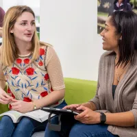 Two female business students sat on a sofa in a discussion