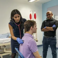 A medicine student uses a stethoscope on a patient while 2 other students watch