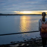 A student gazing reflectively over ƱAPP_ĿͲƱ-ٷϷ, docks as the sun sets over the horizon in the distance.