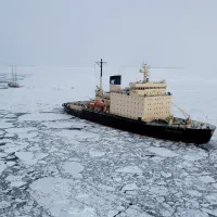 A ship surrouded by ice next to a small vassel.