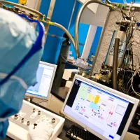 A researcher analysing a complex electrical circuit on a monitor in a cleanroom.