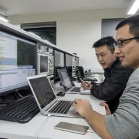 Two cyber security researchers work at a bank of computer screens