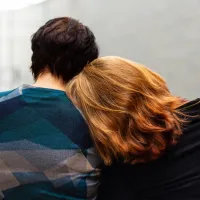 Two people sitting down, facing away from us. One is leaning into the other.