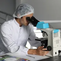 A researcher in a white lab coat looks through a microscope.