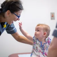 Baby reaches up towards smiling research nurse 