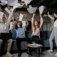 A diverse group of business people throw sheets of paper in the air