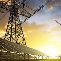 A low-angle view of solar panels, a wind turbine and a pylon, with the sun rising in the background